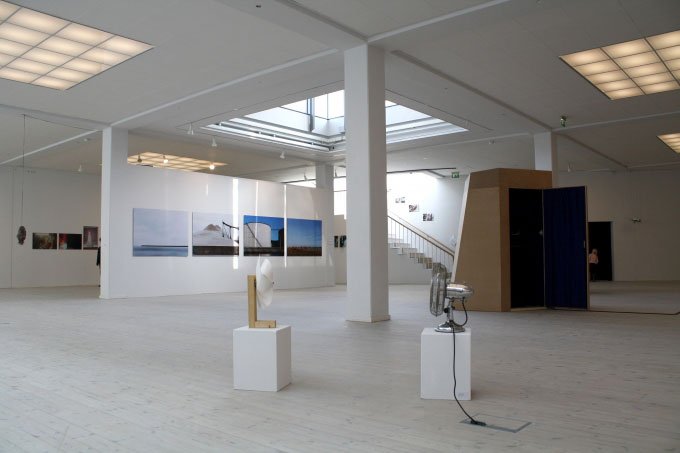 Udstillingsvue: Alexander Thiemes installation Indflydelse ses foran Ulrik Lunds skulptur og videoboks Warped Spaces Twisted Brains, mens vi i baggrunden kan se Morten Barkers fire fotografier Le Vol Des Oiseaux 1-4. Foto: Pernille B.
