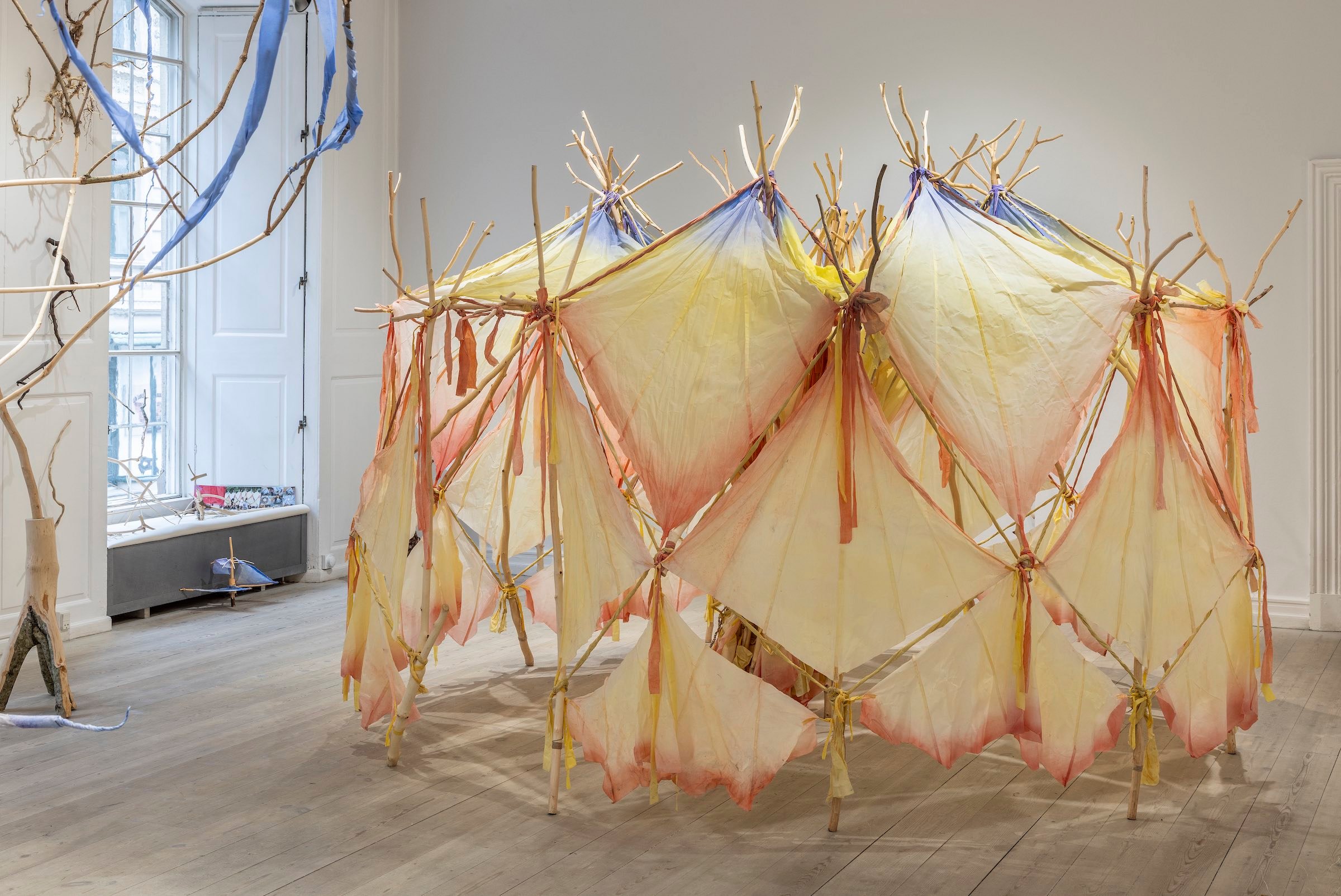 <i>TUSINDBENSTELTET</i>, 2023. Udviklet til børnene på Kærbyskolen i Ålborg, 2023. Gaffelgrene af ahorn og bøg, afbarkede. Sammenbundet med bivoksede, plantefarvede bomuldsrester. Duge af indkøbt bivokset bomuld, gnedet med naturpigmenter. Motivet er en larve, som går og ruller sig sammen. Foto: Ole Akhøj