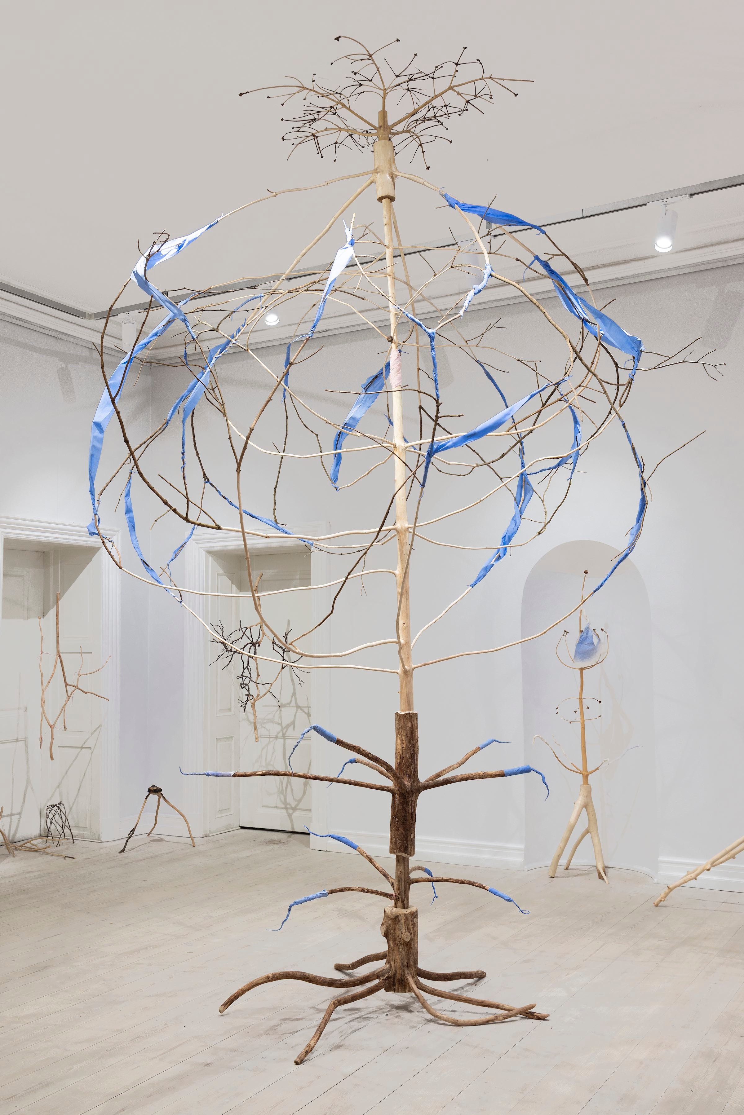 <em>SKOVRUMSSØJLE</em>, 2025. Stamme med grene, afbarket og opdelt, udboret og samlet. Forbundet opad og nedad til store cirkelslag. Forbundet med hinanden med mandelformede bånd, gnedet med naturligt pigment og snoet om grenene. Foto: Ole Akhøj