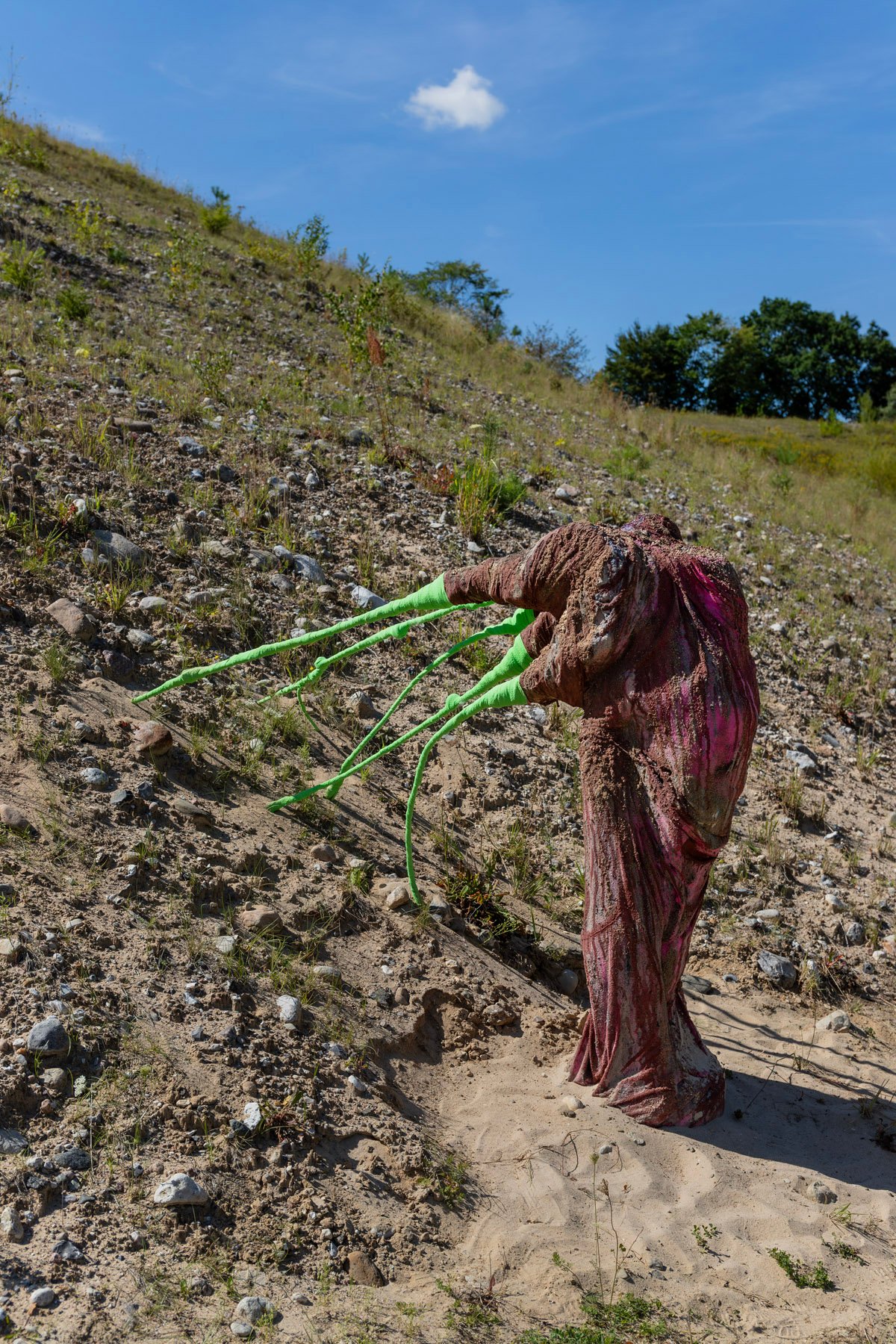 REGITZE ENGELSBORG KARLSEN, IMELLEM SANDET, 2025. Aflagte og brugte tekstiler fra borgerne i Sorø: håndklæder, duge, lagner, dynebetræk og stofrester. Sten i forskellige størrelser, sand og grus. Neongrønt elastik sportstape og et venindearmbånd.