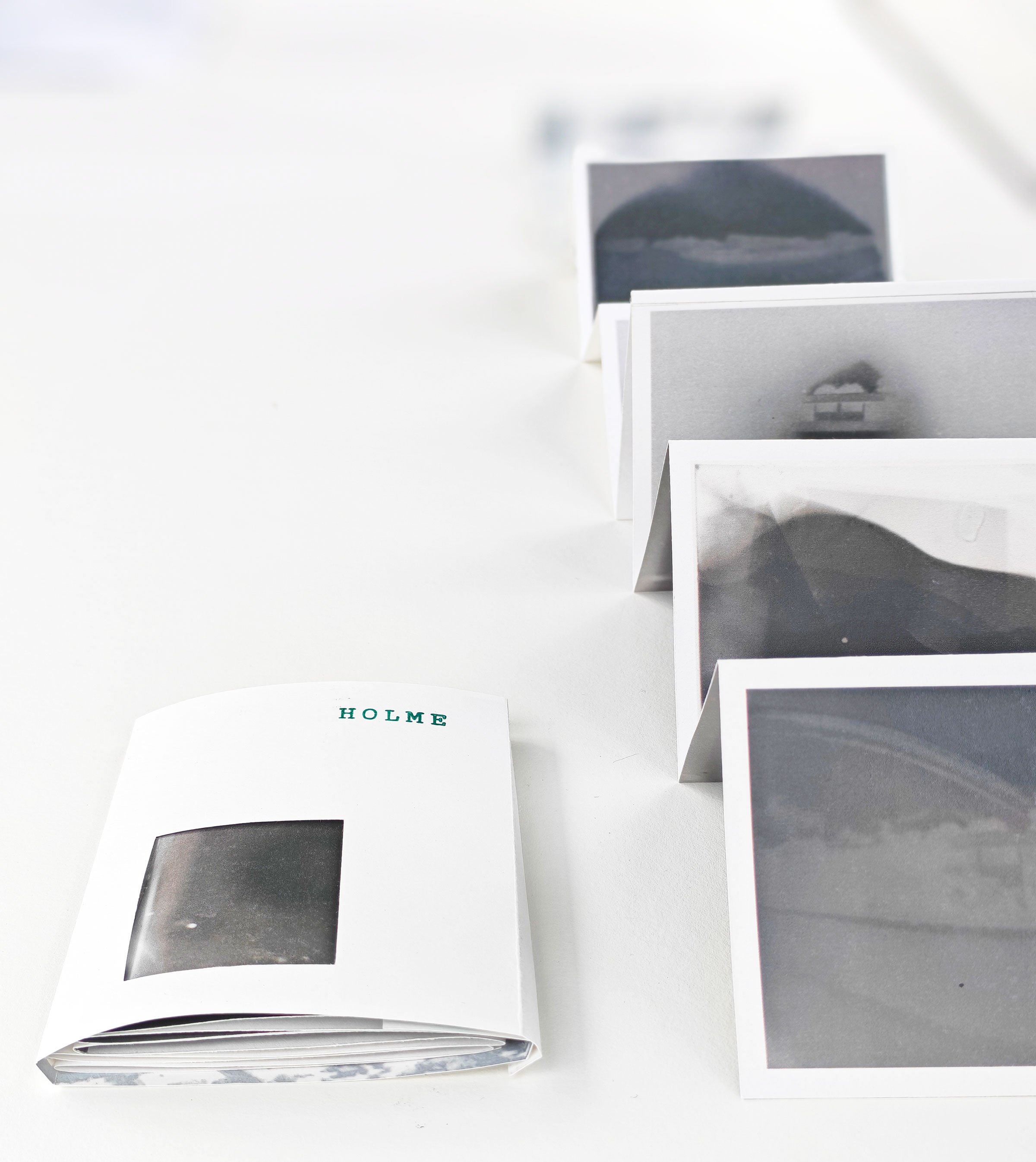 Installationsview, I skiftende lys, hOLME kUNSTHAL, 2026. Ti udvalgte registreringer er samlet i en lille souvenirmappe hvor indersiden af mappen indeholder et historisk kort over Holme. Foto: Sille Juline Høgly Petersen og Ane Bonde Rolsted.